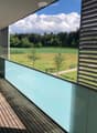 Modern balcony with wooden decking, glass railing, and scenic countryside view.