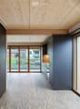 Open-plan unfurnished space with wooden ceiling and floor, large glass doors leading to outdoor view, grey walls, and minimal built-in cabinetry.