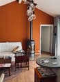 Orange walls, a white sofa with decorative pillows, a round wooden coffee table, a wooden chair, a fireplace, and a black lamp.