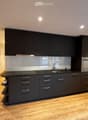 modern kitchen with black cabinets, wooden floor, black countertop, sink, faucet, integrated oven