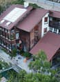 A multi-story residential building with red-tiled roofs, wooden balconies, and a garden area. The structure includes multiple levels with large windows and outdoor spaces.
