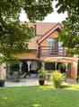 Garden area with a patio, outdoor furniture, umbrella, and a view of the house with a balcony and large windows.