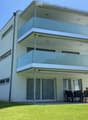modern white building, 3 stories, multiple balconies, glass windows, outdoor dining area