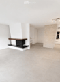Open-plan living space with a fireplace, white walls, grey tiled floor, and recessed lighting. The room is unfurnished, showing only the fireplace and a doorway leading to another area.