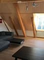 Modern living room with wooden slanted ceiling, large window, grey sectional sofa, coffee table, TV stand, and additional table.