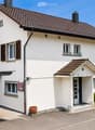 Two-story white house with a tiled roof, multiple windows with shutters, a garage, and a small entrance porch.