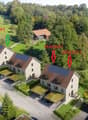 Aerial view of a residential area with multiple houses, green lawns, trees, and driveways. Some houses have solar panels on the roofs.