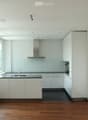 Modern, minimalist kitchen with white cabinets, a central island, and large windows offering a view of greenery. Features include a stainless steel range hood, a built-in oven, and a sleek black countertop.