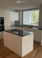 Modern kitchen with white cabinets, black countertops, an island, and built-in oven. Large window provides natural light.