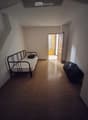 A small, furnished room with a single bed, a suitcase, and an open doorway leading to another room.