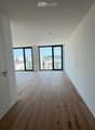 Empty hallway with wooden flooring, white walls, and large windows at the end leading to an outdoor area.