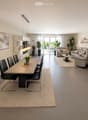 Open-plan living and dining area with modern furniture, pendant lights, and large windows leading to a balcony.