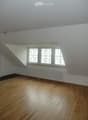 Empty room with wooden flooring, white walls, and large windows with white frames. A radiator is visible below the windows.