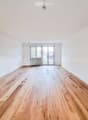 Empty room with wooden flooring, white walls, and large glass doors leading to a balcony.