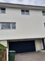 Modern two-story house with white exterior, large windows, and a dark garage door.