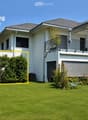 Modern two-story house with white exterior, grey roof, large windows, balcony, and well-maintained garden.