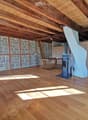 Empty room with wooden flooring, exposed wooden beams, stone walls, and a staircase leading to an upper level. No furniture or equipment is present.