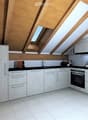 Modern kitchen with white cabinets, stainless steel appliances, and a black countertop. Features include a refrigerator, oven, toaster, and decorative vases.