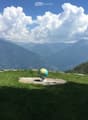 A grassy hilltop with a globe on a stone platform, overlooking a mountain range under a partly cloudy sky.