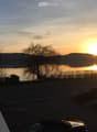 Balcony overlooking a serene lake at sunset, with trees and distant hills visible.