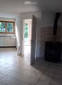 Bright room with tiled floor, fireplace, and an open doorway leading to another room with a window and kitchen area.
