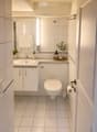 Modern bathroom with white tiles, a sink, a toilet, a mirror, and a small plant on the counter.