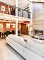 Open-plan living and dining area with a white sectional sofa, coffee table, fireplace, TV, dining table with chairs, and a wooden cabinet.