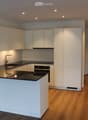 Modern kitchen with white cabinets, black countertop, built-in sink, and oven. Wooden flooring and recessed lighting.
