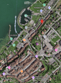 Aerial view of a town with buildings, streets, and a waterfront area with a marina. Visible landmarks include a hotel, school, and recreational areas.