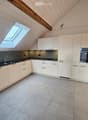 white kitchen cabinets, grey floor tiles, black countertops, stainless steel sink, dishwasher, built-in oven, skylight
