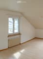 Empty attic room with wooden flooring, white walls, large windows, and a skylight. No furniture or equipment present.