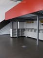 Open-plan unfurnished space with white walls, black floor, white shelving units, and a staircase leading to an upper level.