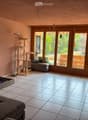 Living room with tiled floor, large windows, cat tree, sofa, television, and a stool.