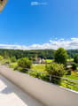 Balcony with tiled floor, metal railing, overlooking a green park area with trees, a playground, and distant mountains.
