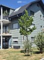 Two-story house with light green siding, multiple windows, balconies, and a small garden area with outdoor furniture.