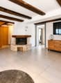 Living room with exposed wooden beams, fireplace, television, wooden cabinet, potted plants, and a rug.