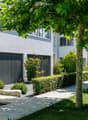 Modern garden with a well-maintained lawn, trimmed hedges, trees, and a wooden deck area near the house.