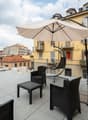 Roof terrace with tiled floor, metal railing, and outdoor furniture including chairs, a table, and a large umbrella.