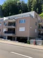 Modern multi-story residential building with balconies, large windows, and a parking area at the base.