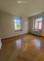 Empty room with wooden flooring, white walls, and two windows with radiators beneath them.