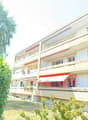 A multi-story residential building with balconies, large windows, and a modern facade. The building is surrounded by greenery and has a well-maintained lawn.