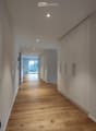 Modern hallway with light wooden flooring, white walls, built-in storage units, and recessed lighting.