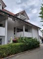 Two-story residential building with white exterior, multiple windows, balconies, and a well-maintained garden area.