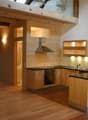 Modern kitchen with wooden cabinets, stainless steel appliances, and a black countertop. Features include a stove, oven, sink, range hood, and built-in lighting.