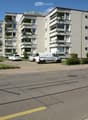 An apartment building with multiple balconies, parking space for several cars.