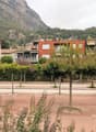A landscaped outdoor area with trees, benches, and modern buildings in the background, set against a mountainous backdrop.