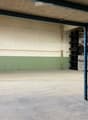 Empty warehouse space with concrete floor, metal shelving units, and storage crates in the background.