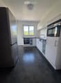 Modern kitchen with white cabinets, stainless steel appliances, dark tiled floor, and a window offering a view of greenery.