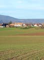 Rural landscape with scattered houses, green fields, and distant mountains under a clear sky.