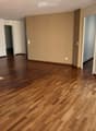Empty room with polished wooden flooring, white walls, and large windows with blinds. No furniture or equipment present.